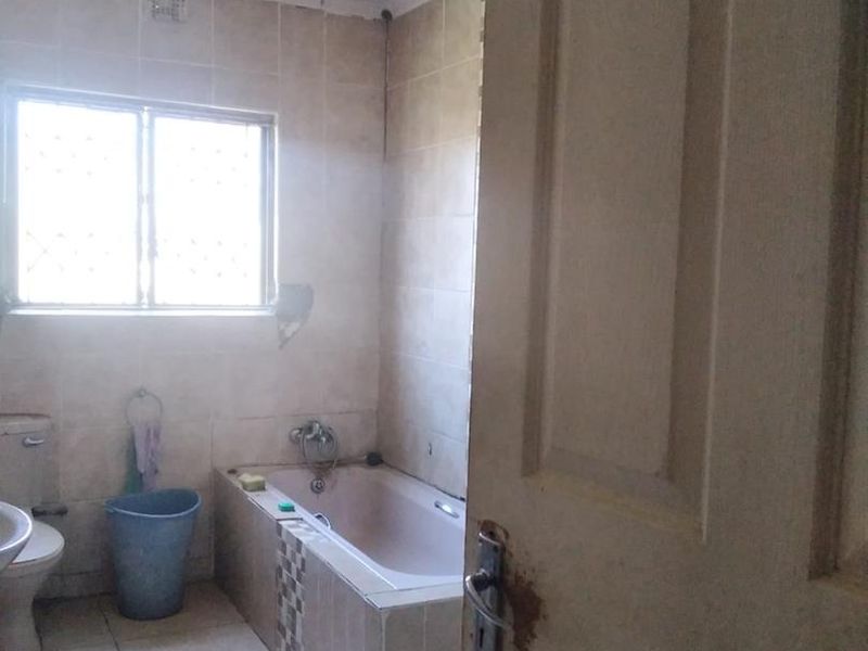 A functional bathroom featuring a built-in bathtub, tiled walls and flooring, and a window with security bars, requiring cosmetic updates.