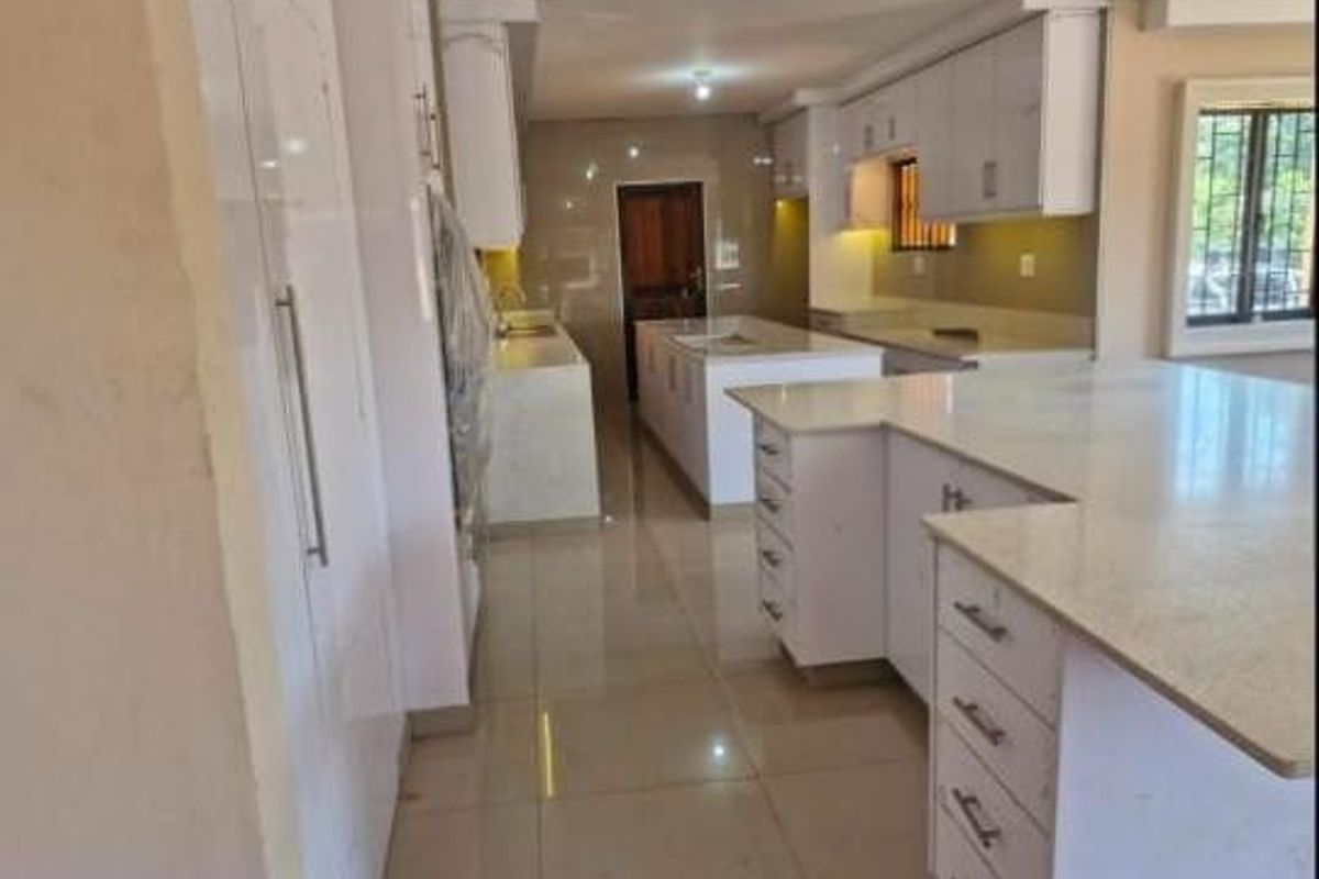 A modern, spacious kitchen featuring white built-in cabinetry, stone countertops, a central island, and polished tiled flooring.