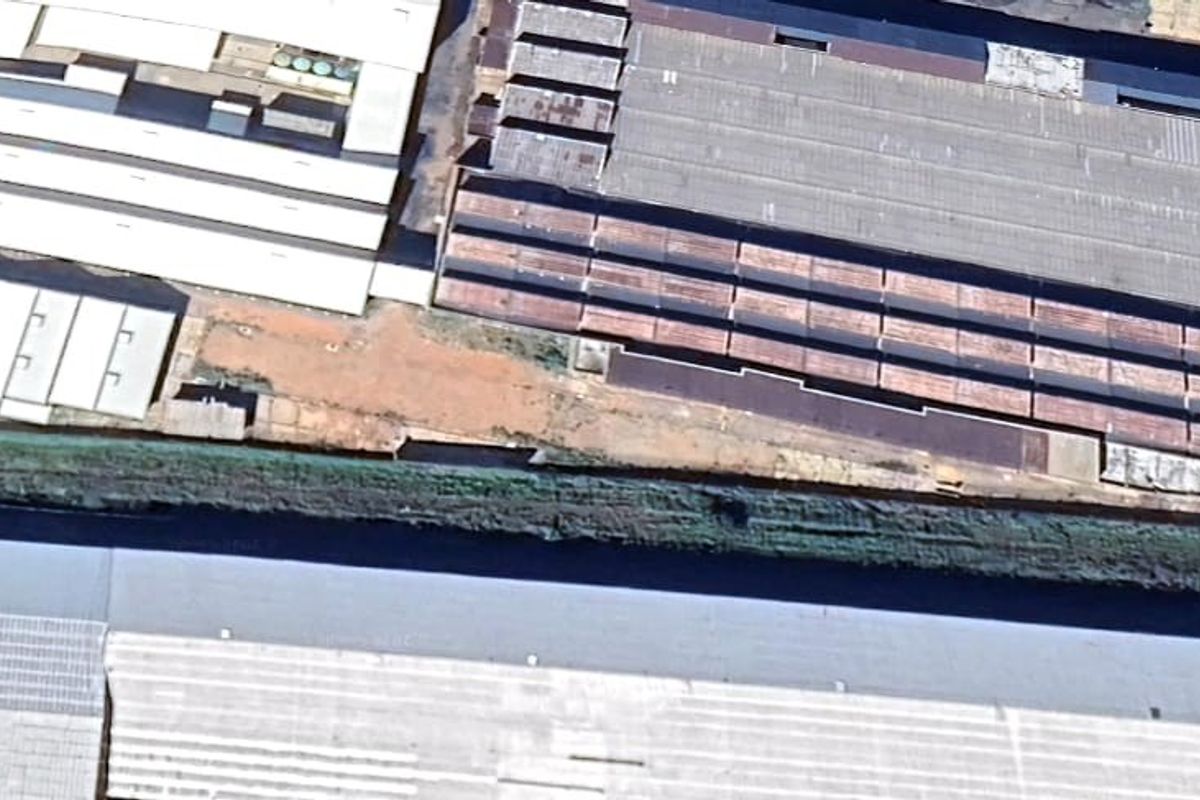 Aerial view of an industrial facility featuring multiple large warehouse structures with corrugated metal roofing and surrounding unpaved yard space.