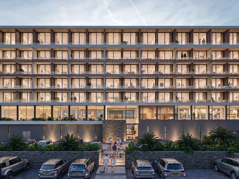 Modern multi-story apartment building facade featuring extensive glass balconies, stone architectural detailing, and a well-lit paved entrance area.