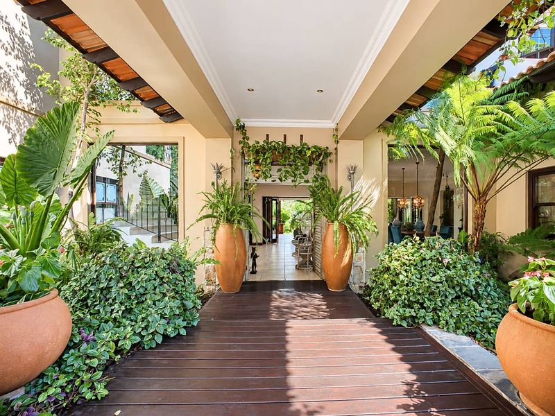 A beautifully landscaped covered entrance walkway featuring timber decking, stone accents, and a welcoming architectural design leading into the home.