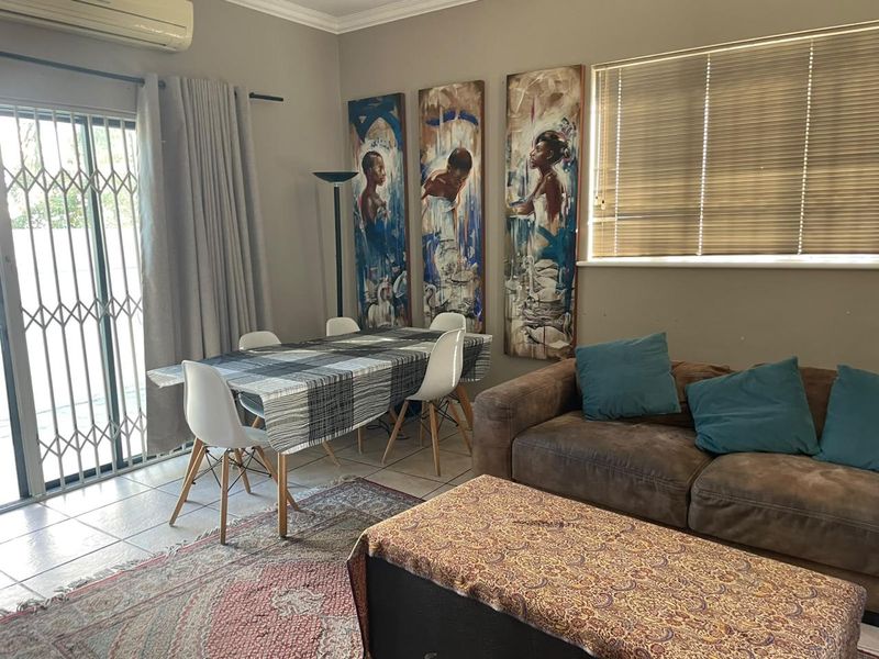 Open-plan living and dining area featuring tiled flooring, a split-system air conditioner, and large sliding glass doors with security gates leading outdoors.