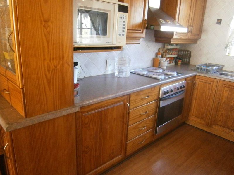 A functional kitchen featuring traditional wooden cabinetry, laminate countertops, built-in oven, electric hob, and a tiled backsplash.