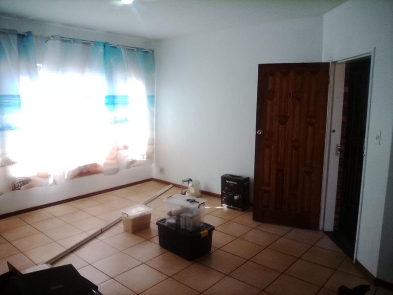 An empty living room featuring tiled flooring, a wooden door, and a window with natural light.