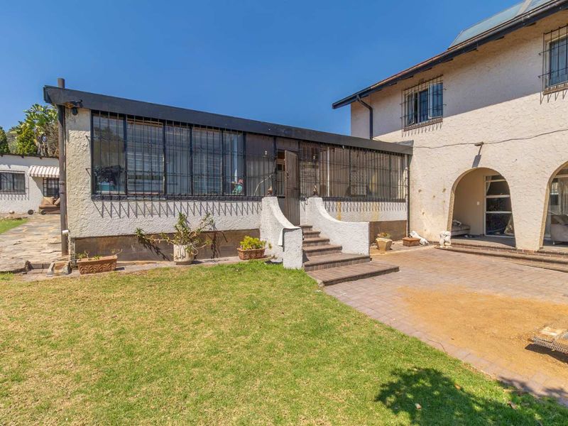 Rear view of the property featuring a paved patio area, lawn, and an arched entrance leading into the home.