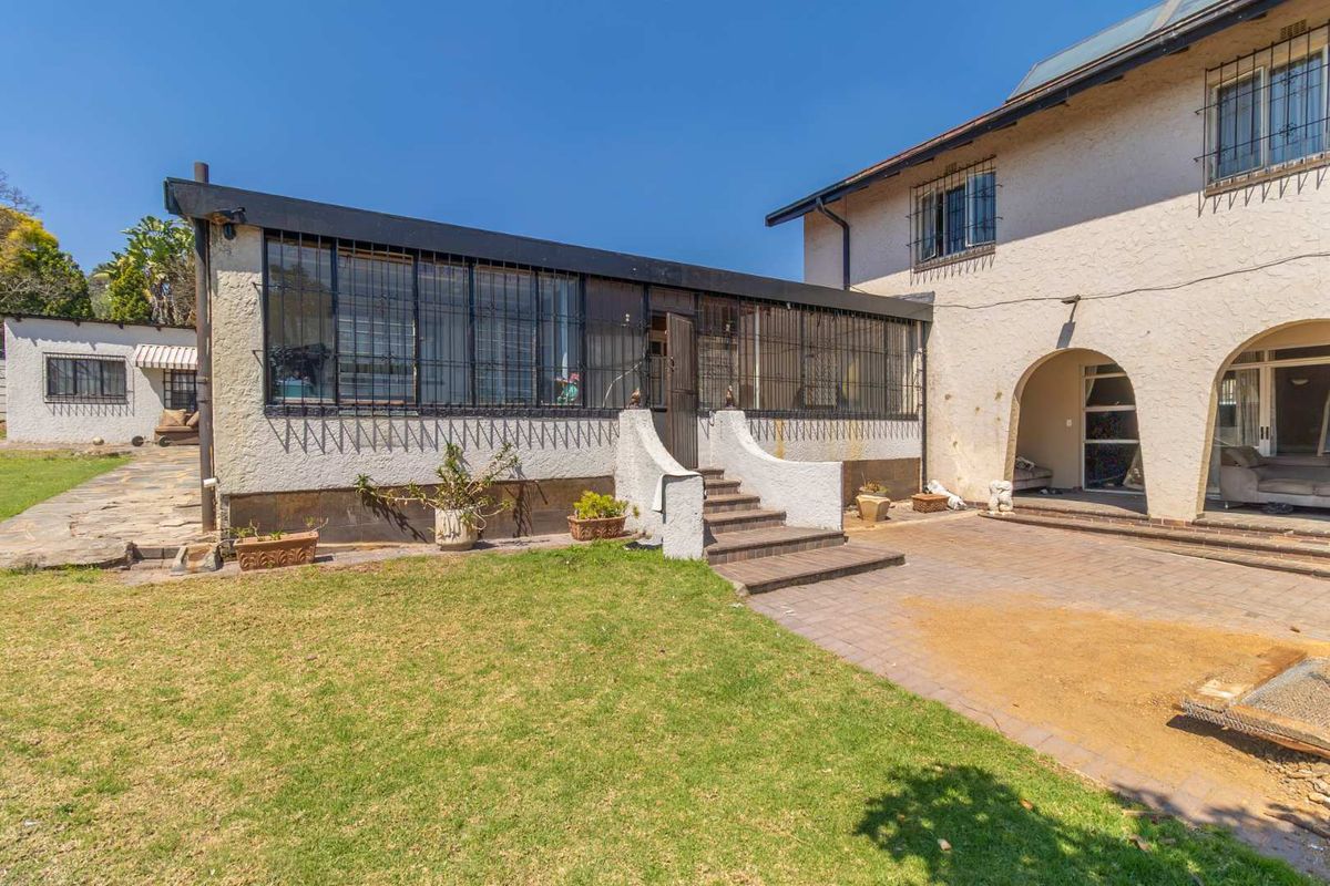 Rear view of the property featuring a paved patio area, lawn, and an arched entrance leading into the home.