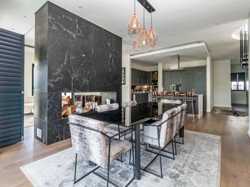 Modern open-plan living and dining area featuring a striking marble-clad double-sided fireplace, hardwood floors, and a sleek, fully equipped contemporary kitchen.
