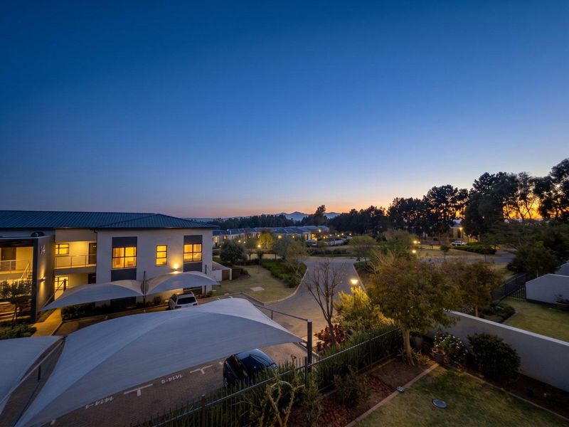 An elevated evening view of the apartment complex grounds, featuring paved parking areas with shade sail structures and well-maintained landscaped gardens.