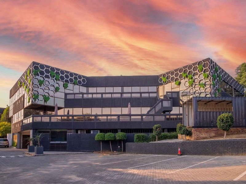 Modern office building exterior featuring a unique honeycomb facade design, integrated vertical greenery, and a spacious paved parking area.