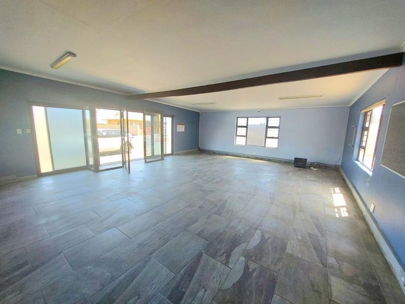 Spacious, open-plan living area featuring large windows, tiled flooring, and sliding glass doors providing ample natural light and direct access to the exterior.