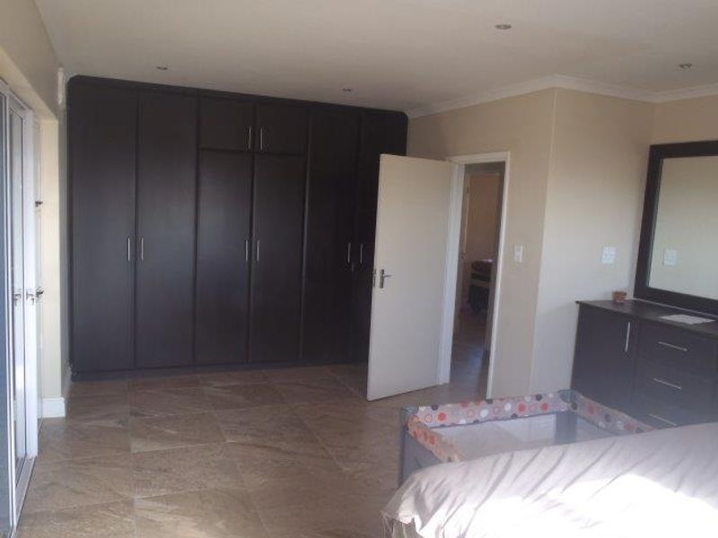 Spacious bedroom featuring extensive dark wood built-in cupboards, neutral wall finishes, and durable tiled flooring with recessed lighting.