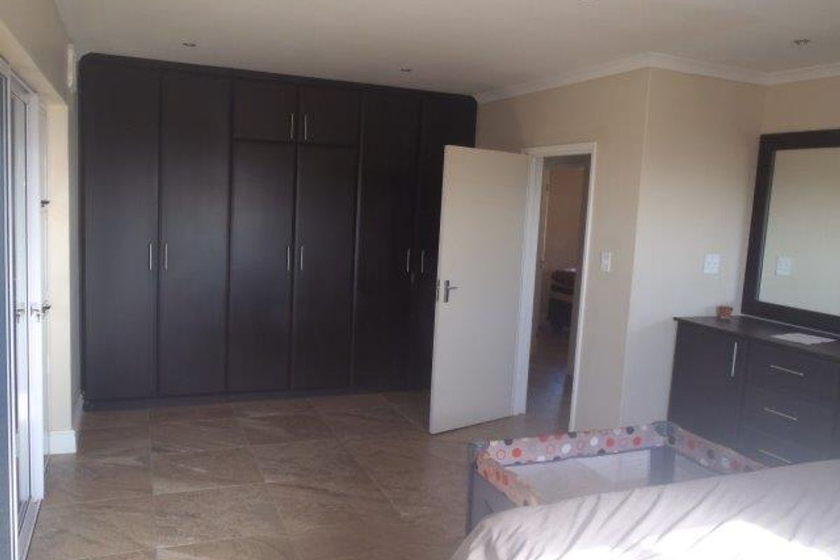 Spacious bedroom featuring extensive dark wood built-in cupboards, neutral wall finishes, and durable tiled flooring with recessed lighting.