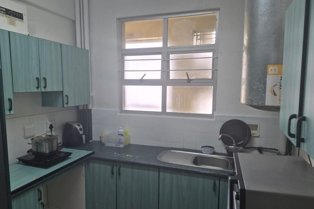 A functional kitchen featuring laminate cabinetry, a stainless steel sink, and a tiled splashback, offering a practical layout with potential for modern updates.