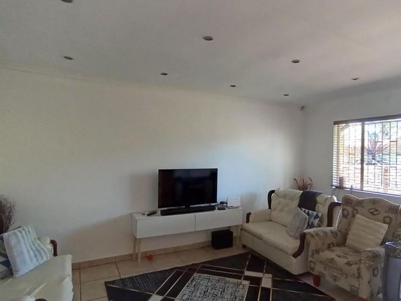 A bright living room featuring tiled flooring, recessed downlighting, and a large window fitted with security bars and venetian blinds.
