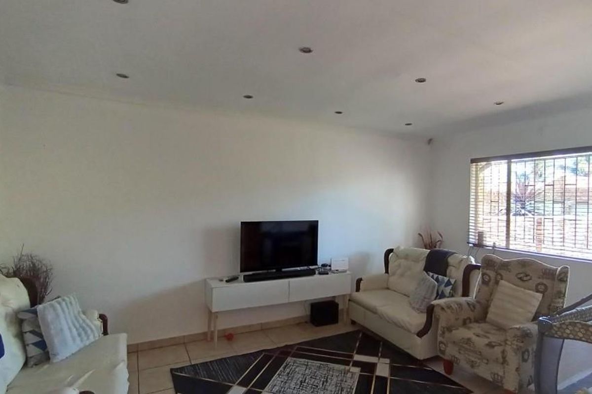 A bright living room featuring tiled flooring, recessed downlighting, and a large window fitted with security bars and venetian blinds.