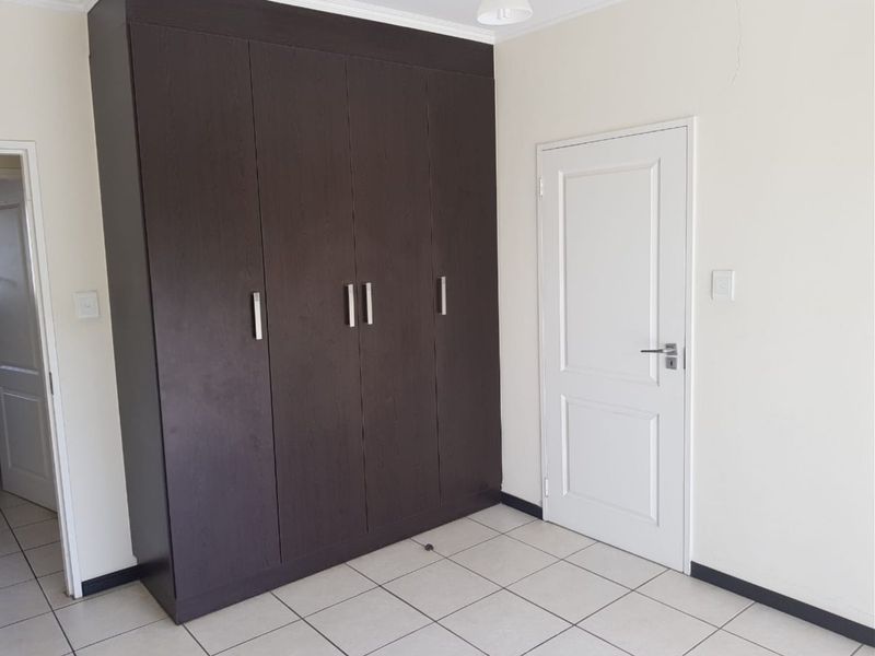 A clean, empty bedroom featuring dark wood built-in wardrobes, neutral tiled flooring, and white walls, providing a blank canvas for personalization.