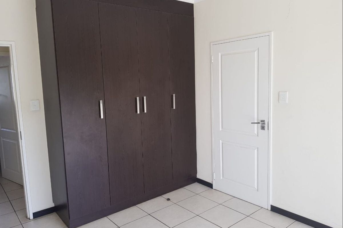A clean, empty bedroom featuring dark wood built-in wardrobes, neutral tiled flooring, and white walls, providing a blank canvas for personalization.