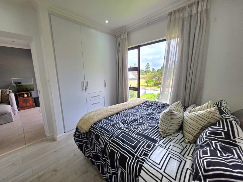 A well-maintained bedroom featuring built-in cupboards, light laminate flooring, and large windows providing natural light and exterior views.