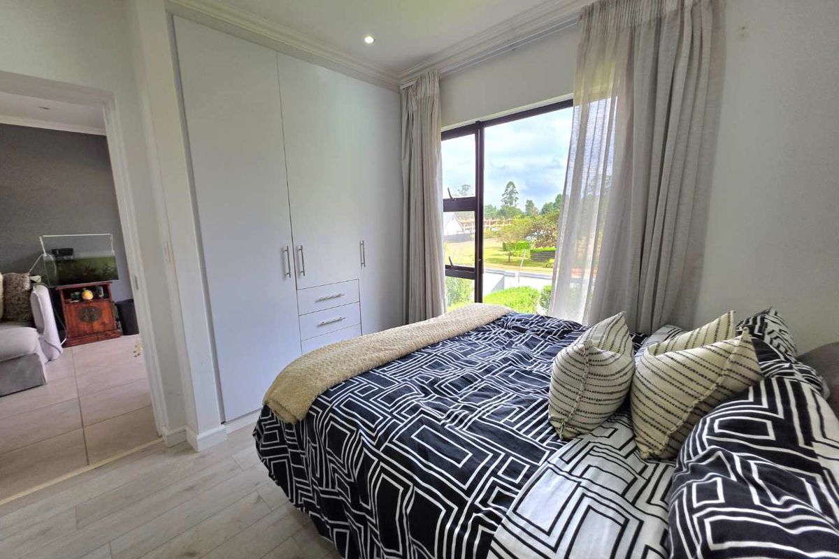 A well-maintained bedroom featuring built-in cupboards, light laminate flooring, and large windows providing natural light and exterior views.