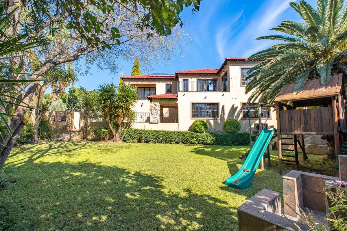 A spacious rear garden featuring a well-maintained lawn, mature landscaping, and a view of the two-story residential building with a tiled roof.