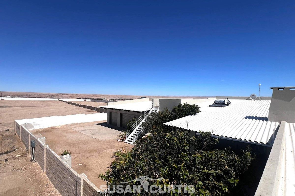 Aerial view of the property showing the corrugated metal roof, solar geyser, external staircase, and surrounding fenced yard area with expansive landscape views.