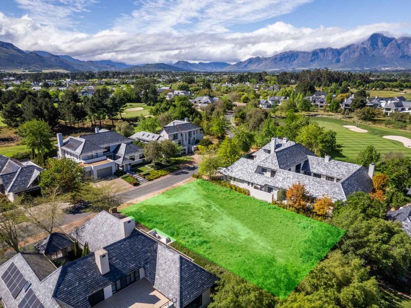 An aerial view of a vacant residential plot situated within a well-established estate, surrounded by luxury homes and scenic mountain views.
