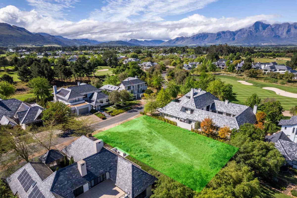 An aerial view of a vacant residential plot situated within a well-established estate, surrounded by luxury homes and scenic mountain views.