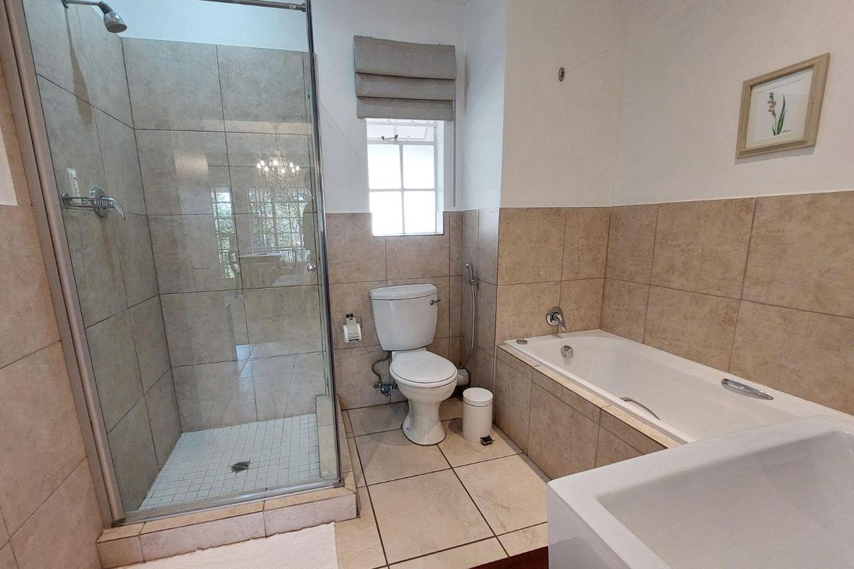 A well-maintained bathroom featuring a glass-enclosed shower, a separate bathtub, a toilet with a bidet spray, and neutral floor-to-ceiling tiling.