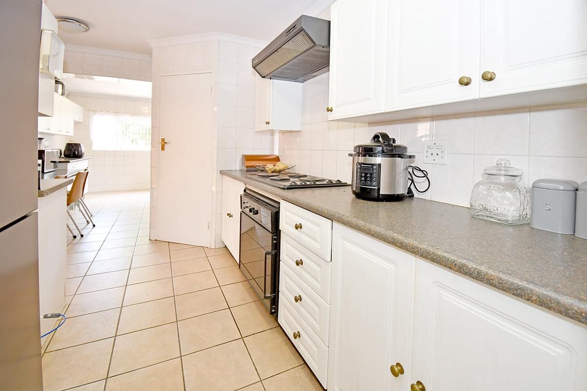 A functional kitchen featuring white cabinetry, tiled flooring, a built-in oven, and a hob with an extractor fan.