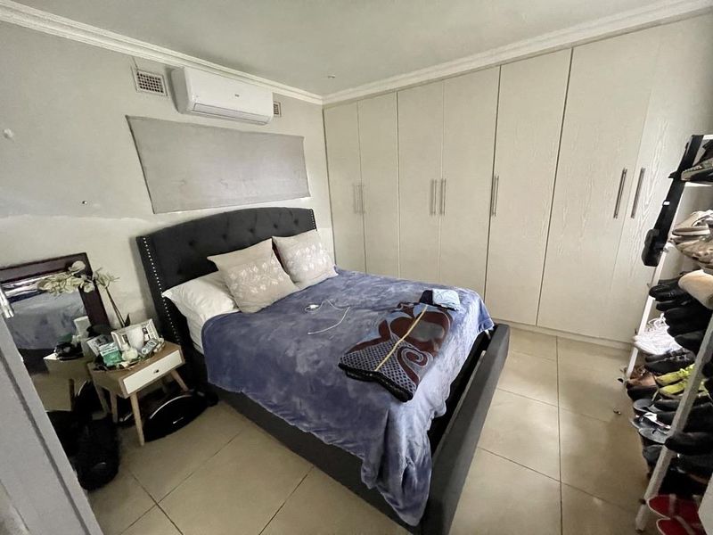 Bedroom featuring tiled flooring, extensive built-in cupboards, and a wall-mounted air conditioning unit.