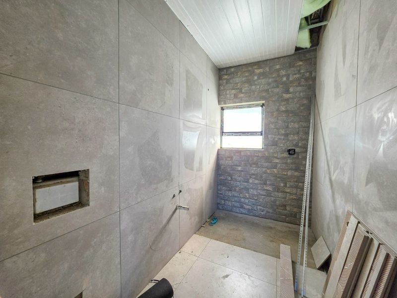 An unfinished bathroom space currently under renovation, featuring large format grey wall tiles, a stone-clad feature wall, and exposed plumbing ready for final fixtures.