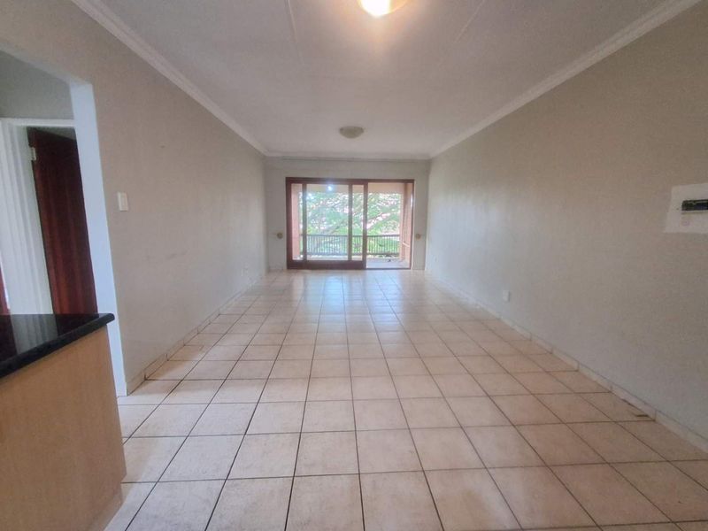 An empty open-plan living area featuring tiled flooring and a large sliding glass door providing access to an outdoor balcony.