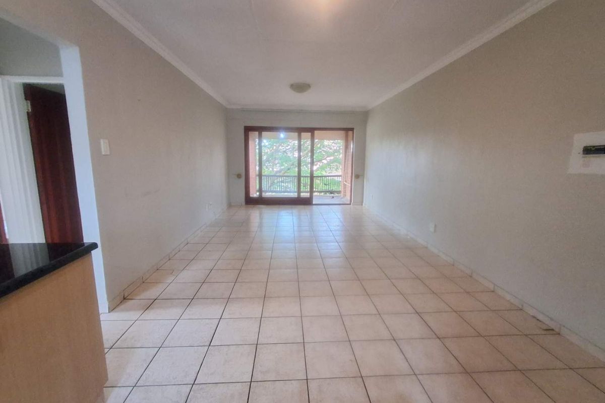 An empty open-plan living area featuring tiled flooring and a large sliding glass door providing access to an outdoor balcony.