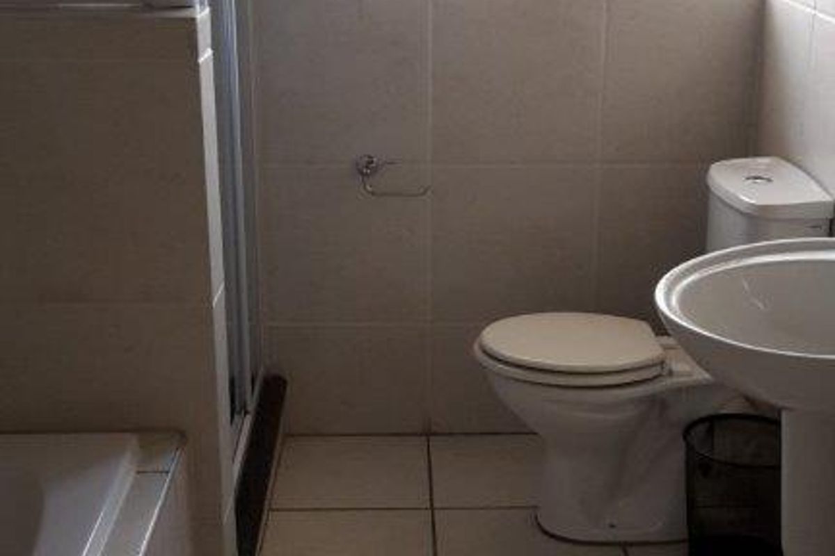 A functional bathroom featuring a shower enclosure, pedestal basin, and toilet, finished with neutral wall and floor tiles and fitted with venetian blinds.