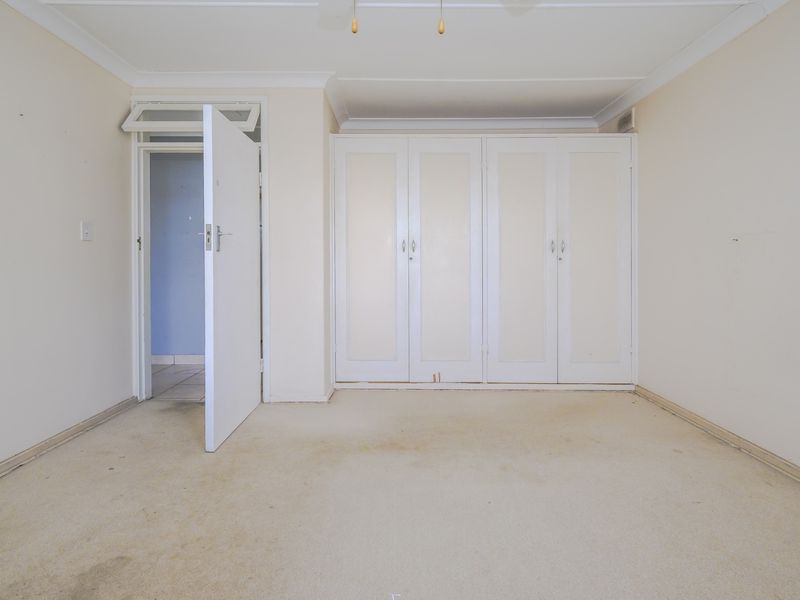 An empty bedroom featuring built-in cupboards, carpeted flooring, and coved ceilings, offering a blank canvas for renovation or restyling.