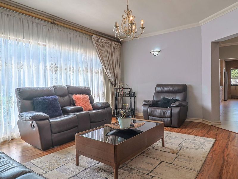 Spacious living room featuring laminate flooring, elegant chandelier lighting, and large windows with sheer curtains, leading through to an open-plan kitchen area.