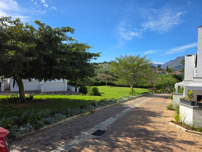 A well-maintained front exterior view of the townhouse featuring a paved driveway, double garage, and a lush, landscaped garden with mountain views.