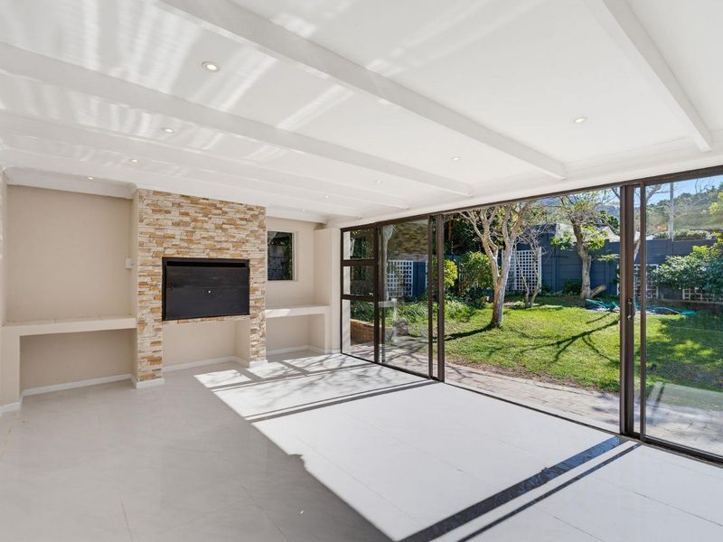 Bright and spacious living area featuring a stone-clad built-in fireplace, recessed lighting, and large sliding glass doors opening to the garden.
