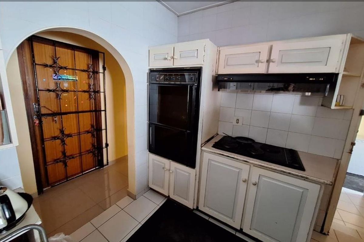 A dated kitchen featuring built-in oven, hob, extractor fan, and tiled splashbacks, with an arched doorway leading to an adjacent area.