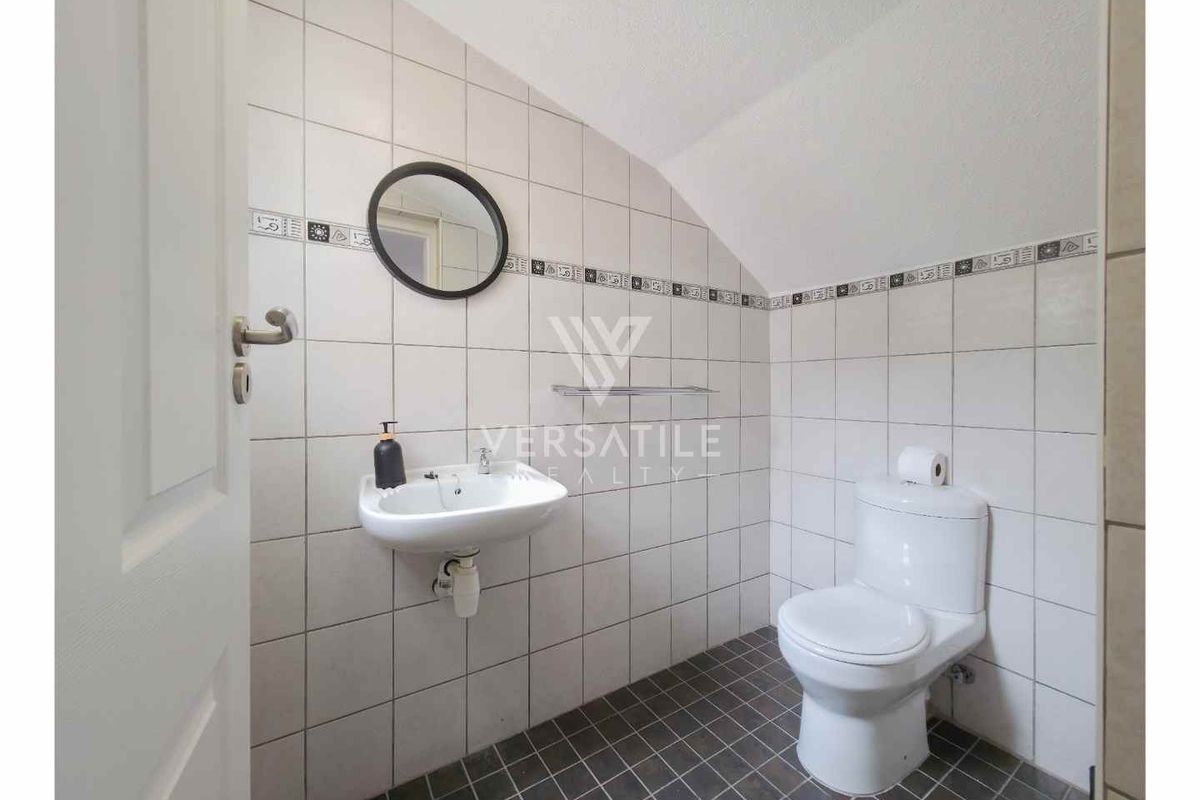 A compact bathroom featuring a wall-mounted basin, a standard toilet, and full-height wall tiling with a decorative border.