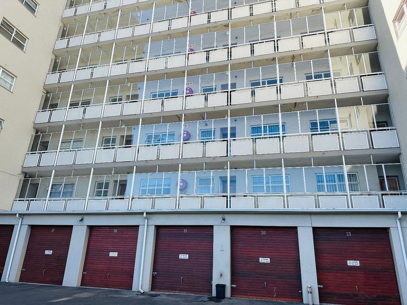 Exterior view of a multi-story apartment building featuring enclosed balconies and a row of ground-level garages.