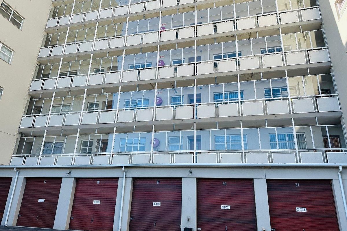 Exterior view of a multi-story apartment building featuring enclosed balconies and a row of ground-level garages.
