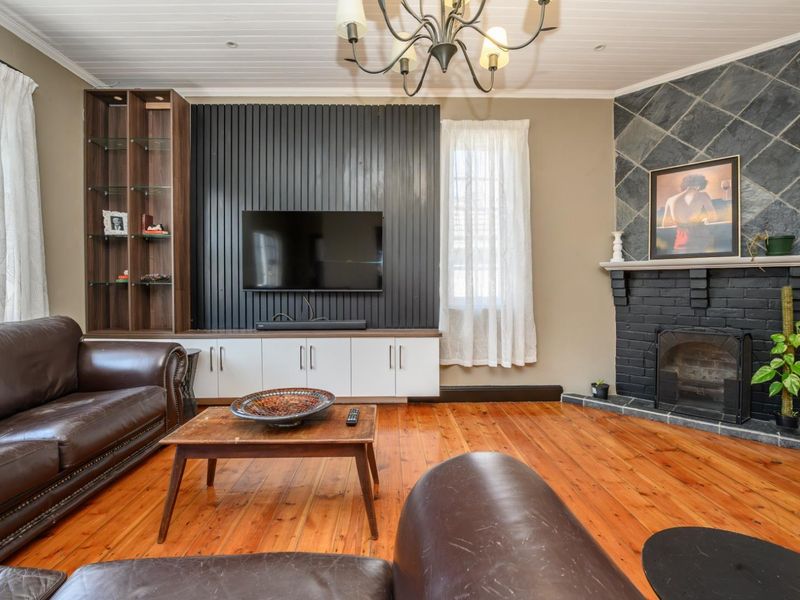 A cozy living room featuring polished timber floors, a built-in media unit, and a characterful fireplace with a slate surround.