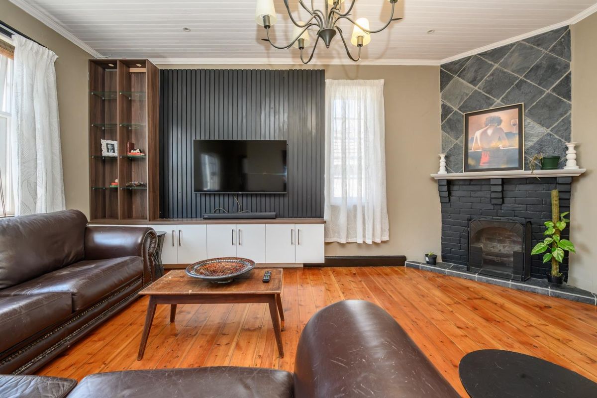A cozy living room featuring polished timber floors, a built-in media unit, and a characterful fireplace with a slate surround.