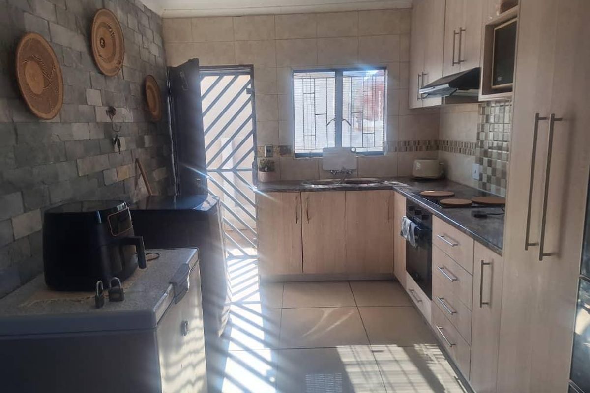 Functional kitchen featuring light wood cabinetry, stone veneer feature wall, tiled backsplash, and direct access to an exterior security gate.