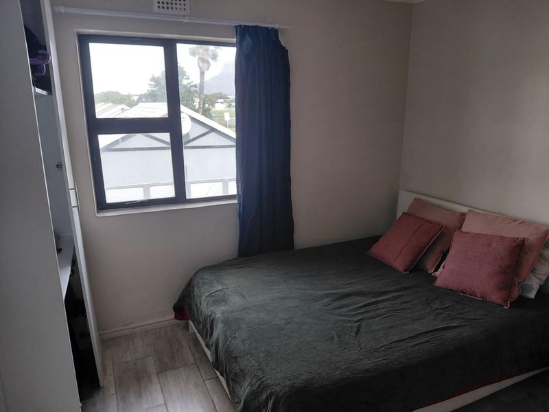 A functional bedroom featuring tiled flooring, a built-in wardrobe, and an aluminium-framed window with natural light.
