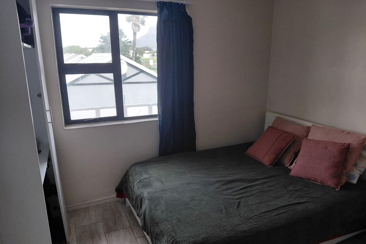 A functional bedroom featuring tiled flooring, a built-in wardrobe, and an aluminium-framed window with natural light.