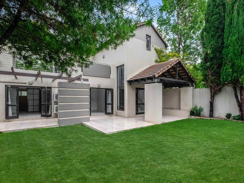 Rear view of the townhouse featuring a tiled patio, pergola, balcony, and a well-maintained private garden.