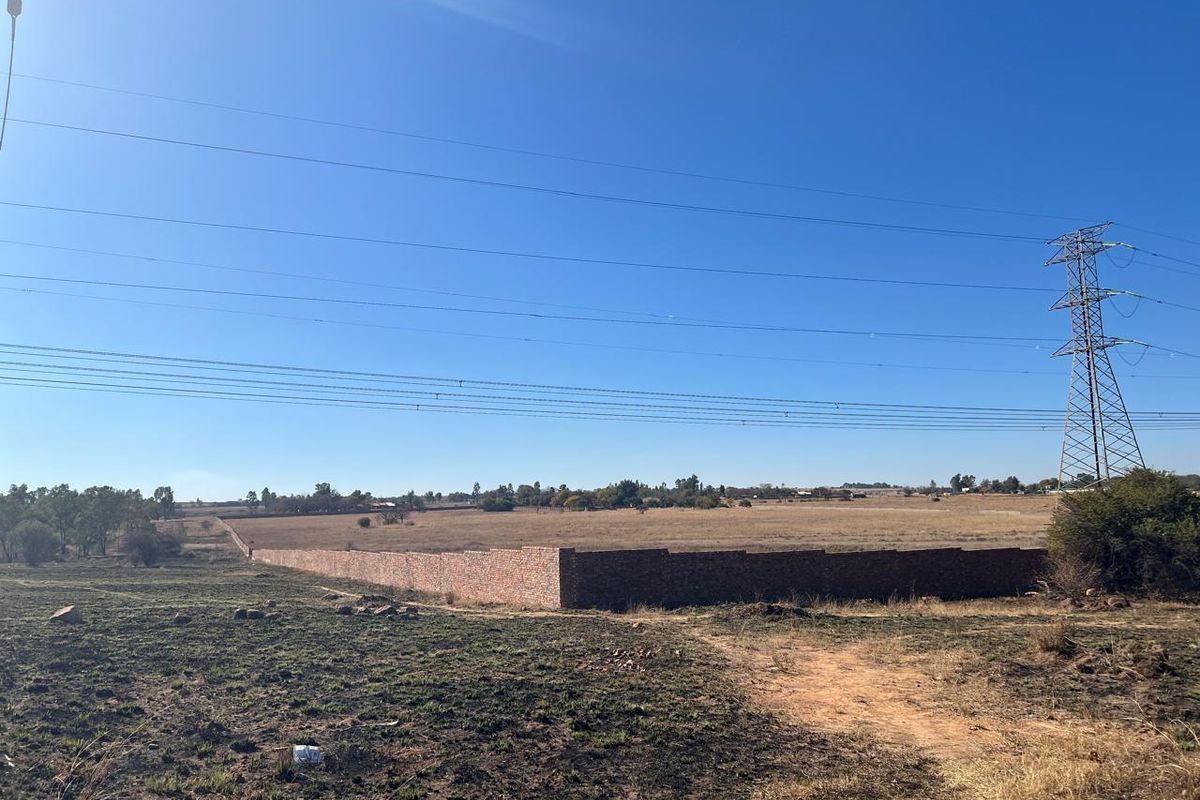 Expansive open farm land featuring a perimeter brick wall and overhead power lines under a clear blue sky.