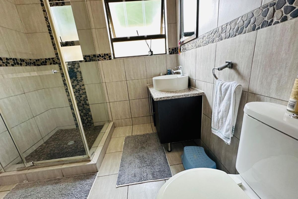 A functional bathroom featuring a glass-enclosed shower, a modern vessel sink on a vanity cabinet, and neutral wall and floor tiling.